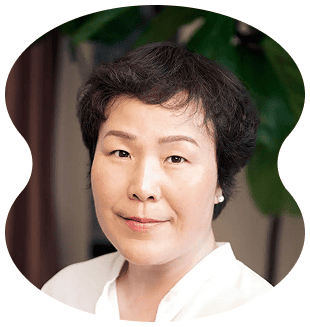 A woman with short, dark hair and a white shirt looks at the camera, with a blurred green plant in the background at Evertrue salon Chicago.
