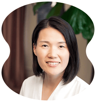 A woman with straight black hair and a white top smiles at the camera inside Evertrue Salon, with a blurred indoor background featuring a green plant.