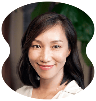 A woman with shoulder-length dark hair and a white top smiles at the camera at Evertrue Salon; a green plant is blurred in the background.