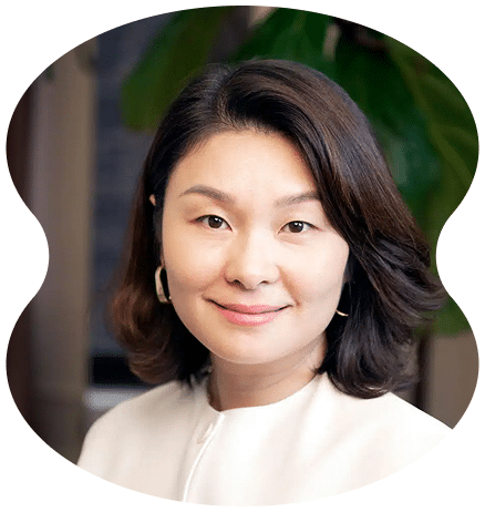 A woman with shoulder-length dark hair, wearing a white top and hoop earrings, smiles at the camera inside Evertrue Salon; a green-leafed plant is blurred in the background.