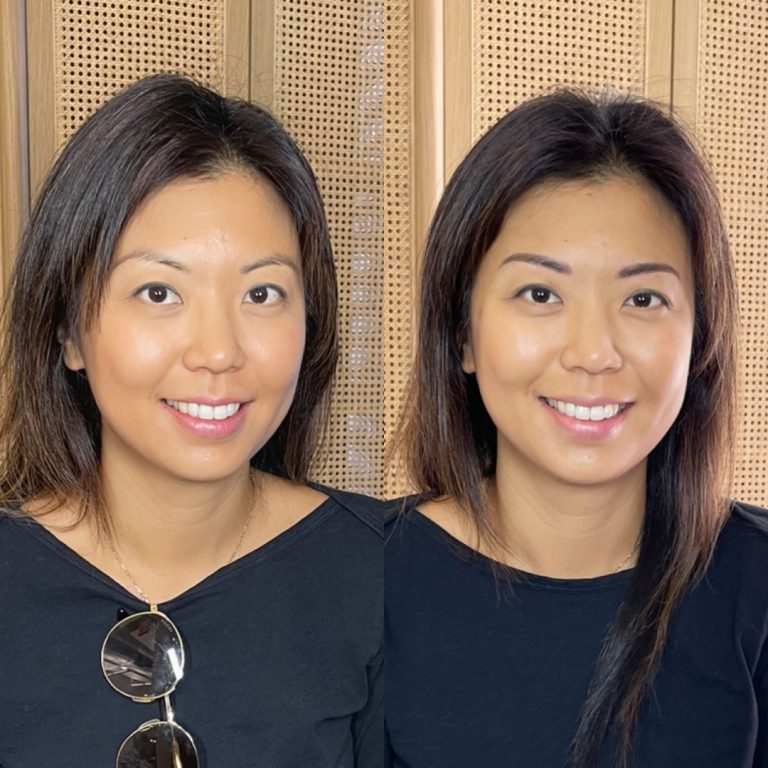 Two women with straight dark hair and similar facial features, both wearing black tops, are sitting side by side in front of a wooden, woven background panel.